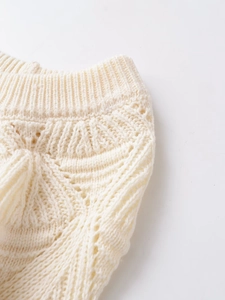 Detail of hollow-out knit pattern and elastic ribbed waist on a cream slim-fit top