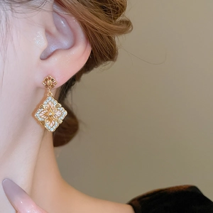 Détail de boucles d'oreilles losanges dorées avec cristaux de zircon et nacre