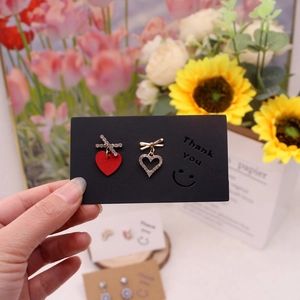 Detail of asymmetric red heart earrings with rhinestones on a black display card