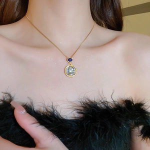 Close-up of a gold chain necklace with a vintage coin pendant and a blue gemstone