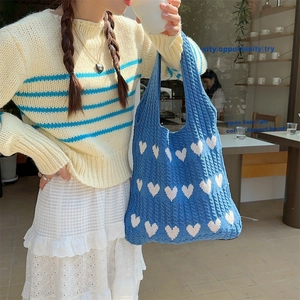 Detailed texture of blue knitted heart tote bag worn by model in a cozy cafe setting