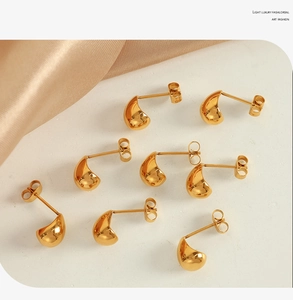 Detailed view of eight golden teardrop stud earrings on white surface with silk fabric
