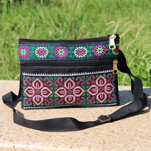 Ethnic crossbody bag with cross stitch embroidery and double zippers on a stone stand