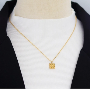 Detail of square embossed chocolate pendant on asymmetric gold chain against a suit