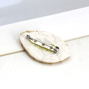 Evil eye embroidery brooch with gold beads and silver pin clasp on textured white fabric