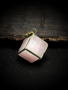 Pink crystal cube pendant with gold-plated edges on a textured dark background