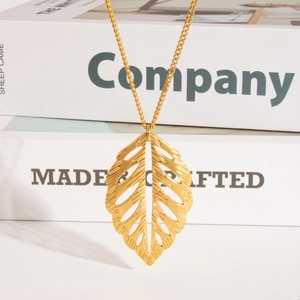 Détail d'un collier avec pendentif feuille ajourée dorée sur un fond minimaliste chic