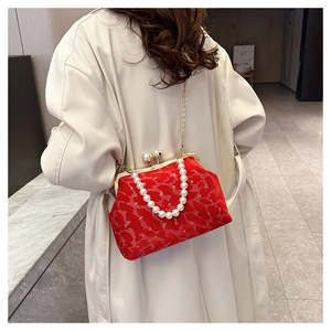 Detail of red velvet shell bag with pearl handle and gold chain worn by a model