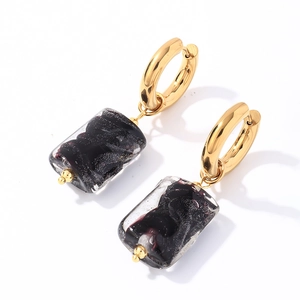 Detailed macro view of gold hoop earrings with dark rectangular stone pendants
