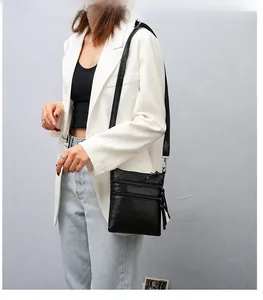 Detail of black PU leather crossbody phone bag with three metal zippers on white blazer