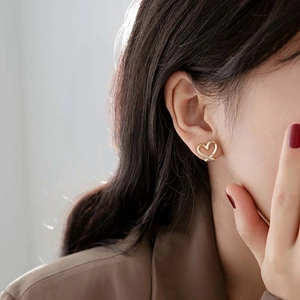 Elegant gold heart-shaped intertwined stud earrings for women on a model's ear