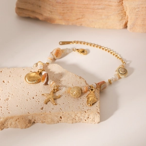 Detail of gold seashell and starfish charm necklace on textured stone props