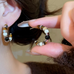 Detailed view of C-shaped earrings with tiger eye beads and silver spacers on ear