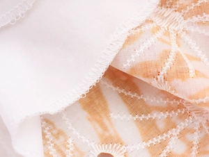 Detalle de tela bordada blanca y naranja claro con costura overlock y textura calada