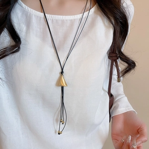 Detailed macro view of a matte gold triangle pendant on a black layered leather cord