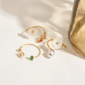 Close-up of gold flower ring with pearls, white shell petals and emerald-cut stones