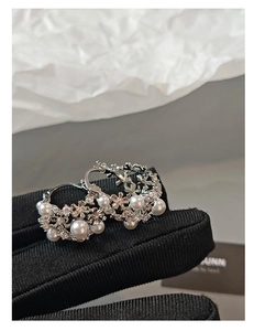 Close-up of silver flower basket earrings with pearls and crystals on black gloves
