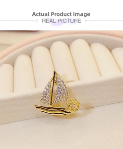 Macro detail of a gold sailboat brooch featuring white pavé crystals and rudder design