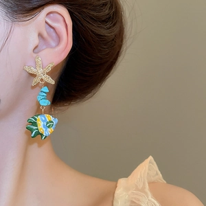Detail of a starfish and colorful glass fish earring worn by a model in close-up view