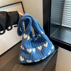 Detailed close-up of blue knitted bag showing white heart patterns and cable textures