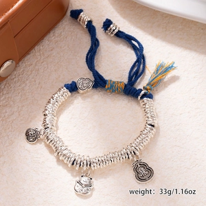 Detail of blue and orange braided bracelet with silver charms on a textured background