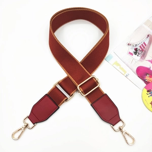 Detail of reddish-brown wide fabric strap with red leather ends and gold metal hooks