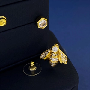 Macro view of gold honeybee earrings with sparkling zircon stones on a navy display