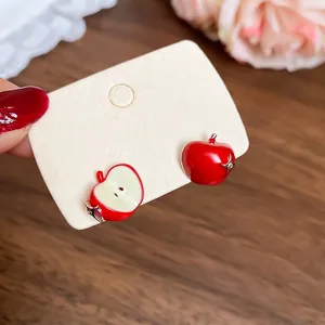Asymmetric red apple stud earrings with enamel finish and silver needles on display
