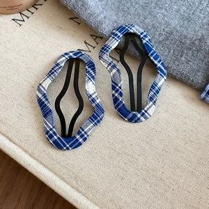 Close-up of blue plaid fabric hair clips with wavy metal frame on beige canvas