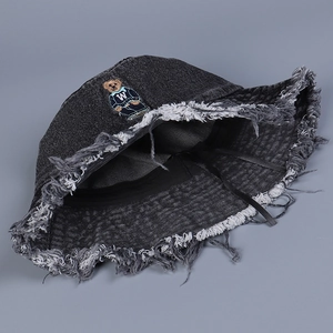 Close-up of embroidered bear patch and distressed frayed brim on denim bucket hat