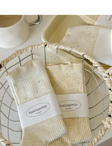 Close-up of Japanese style cream speckled knit socks with ribbed texture in a wire basket