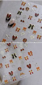 Détail des stickers d'ongles 3D avec nœuds rouges et noirs et coeurs dorés gaufrés