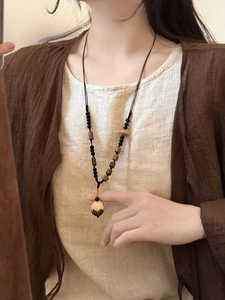 Détail d'un long collier en perles de bois de style chinois avec un pendentif gland naturel