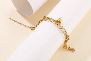 Detail of gold double-layer chain bracelet with heart pendant on white paper roll