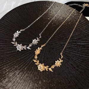 Detailed close-up of gold and silver flower leaf necklaces with cubic zirconia on a dark tray