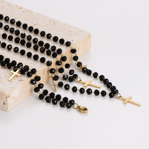 Minimalist rosary necklace with black faceted beads and gold cross pendant on stone