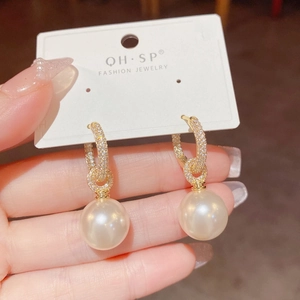 Detail of elegant gold hoop earrings with micro-paved crystals and hanging white pearls