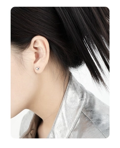 Close-up of heart-shaped silver stud earring on ear showing the polished minimalist finish
