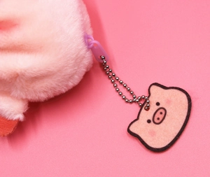 Detail of pink plush coin purse featuring a purple zipper and a small pig tag accessory