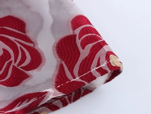 Detailaufnahme von weißem Netzstoff mit roter Blumenstickerei und goldenen Akzenten