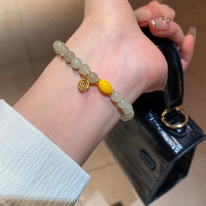 Détail d'un bracelet en perles vert pâle avec un pendentif porte-bonheur doré Fu