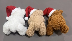 Rear view of three plush Christmas bears in white and brown wearing festive red hats