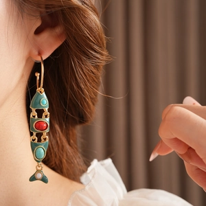 Close-up of vintage golden fish earrings with green enamel on a model's ear