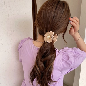 Detail of a beige flower hair claw clip with a pearl center on dark wavy hair