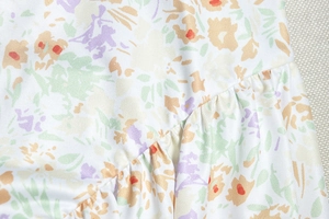 Detailed macro view of white twill fabric with colorful floral print and ruffled hem detail