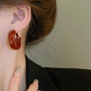 Close-up of retro dark red resin C-shape hoop earrings worn by a model in a blazer