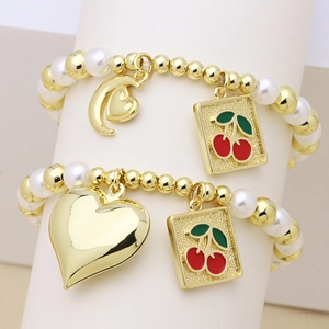 Gold beaded bracelets with pearls featuring heart charms and cherry pendants on a stand