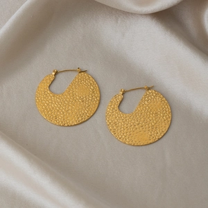 Macro shot of gold-plated hammered hoop earrings with textured finish on satin fabric