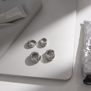 Close-up of four polished stainless steel spring ear cuffs on a minimalist grey background