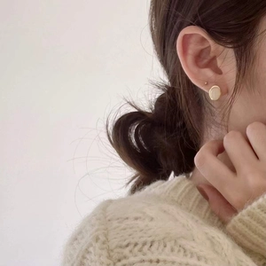 Gros plan d'une puce d'oreille dorée minimaliste avec un pull en maille crème